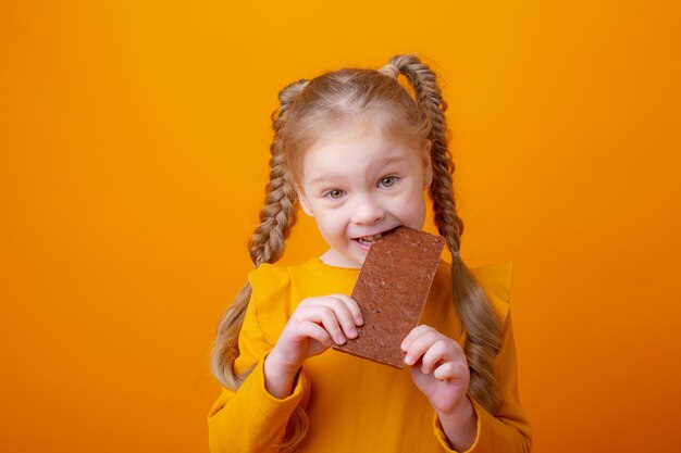 Cute little girl eating chocolate on a yellow background