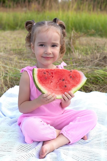 Cute little girl eating watermelon on the grass in summertime