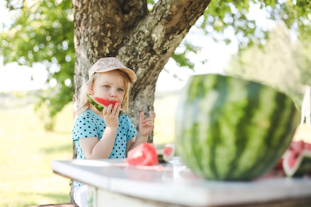 Cute little girl eating watermelon outdoors in summertime Child and watermelon in summer