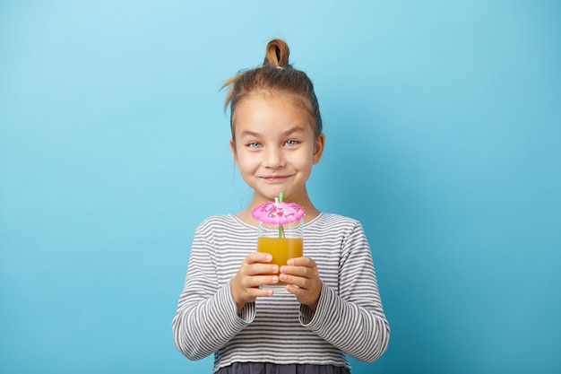 Cute little girl enjoying orange juice on blue isolated background