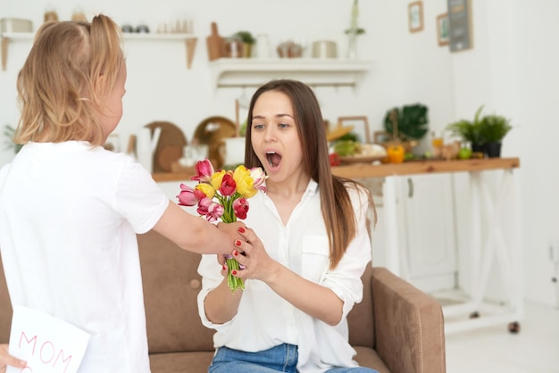 A cute little girl gives flowers and congratulates her mother happy mother's day or March 8