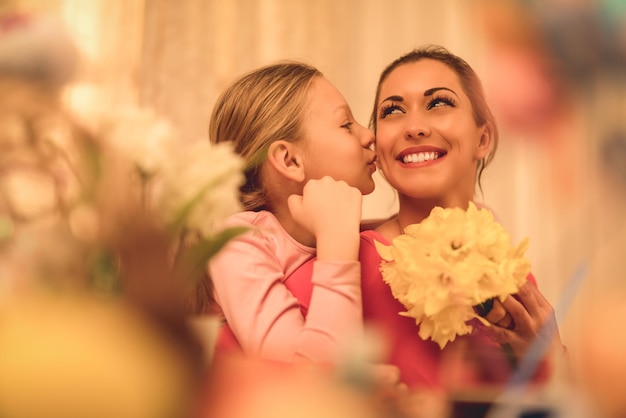 Cute little girl giving her mother bouquet yellow daffodils and kissing you.