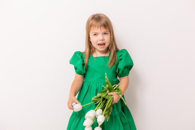 Cute little girl in a green cotton dress with a bouquet of tulips on a light background March 8 mother39s day banner space for text