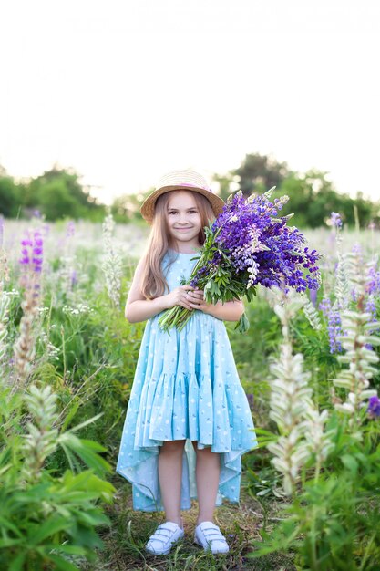 Cute little girl in a hat in a field of lupins.