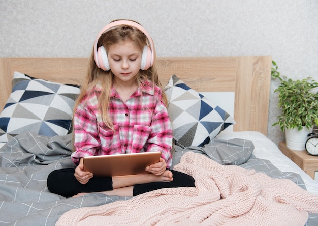 Cute little girl in headphones is using a tablet  at home