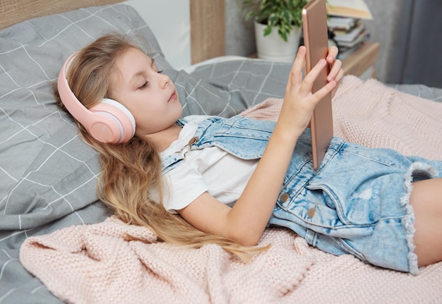 Cute little girl in headphones is using a tablet  at home