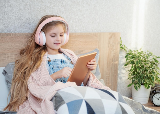 Cute little girl in headphones is using a tablet  at home