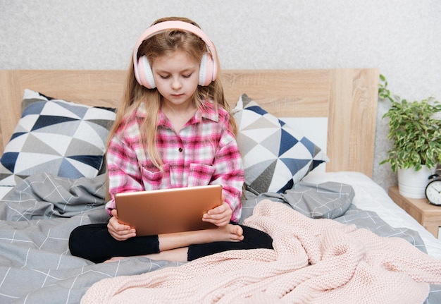 Cute little girl in headphones is using a tablet  at home