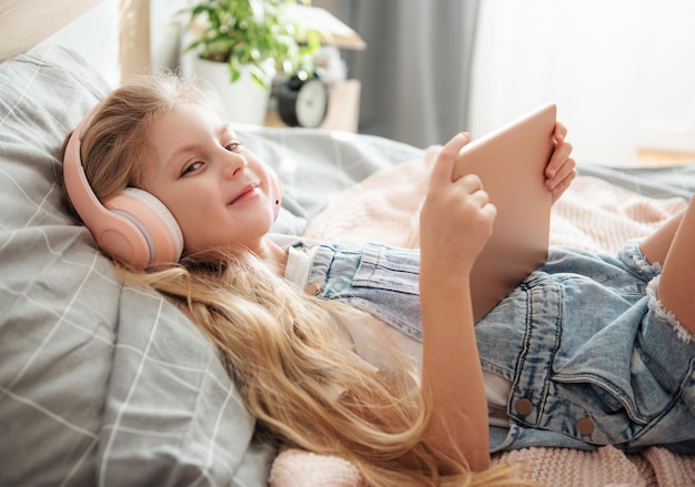 Cute little girl in headphones is using a tablet  at home