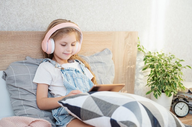 Cute little girl in headphones is using a tablet  at home