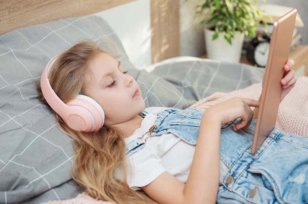 Cute little girl in headphones is using a tablet at home