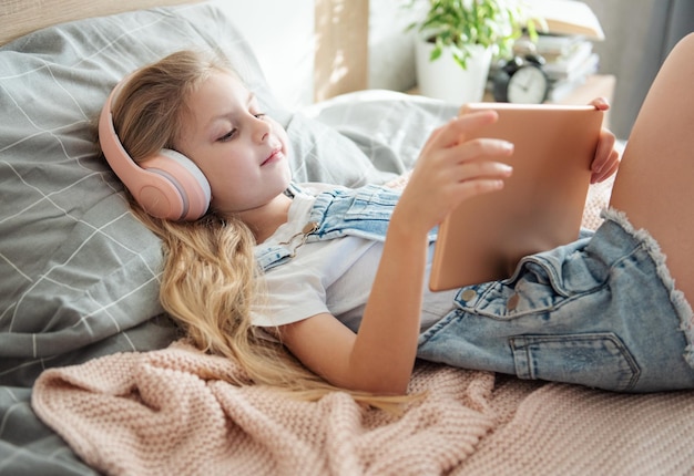 Cute little girl in headphones is using a tablet at home