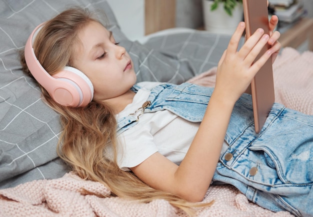 Cute little girl in headphones is using a tablet at home