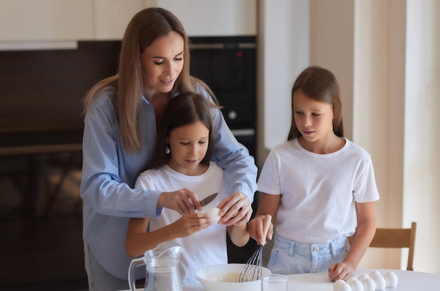 Cute little girl and her beautiful mom in aprons are playing and laughing while kneading the dough in the kitchen