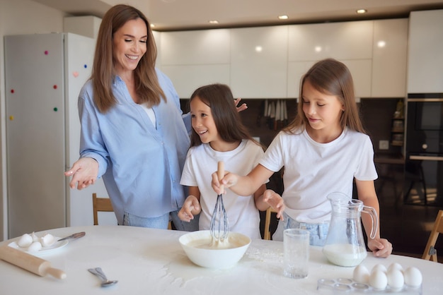 Cute little girl and her beautiful mom in aprons are playing and laughing while kneading the dough in the kitchen