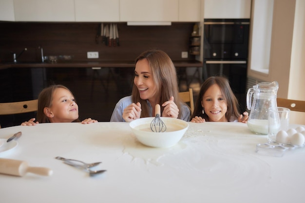 Cute little girl and her beautiful mom in aprons are playing and laughing while kneading the dough in the kitchen