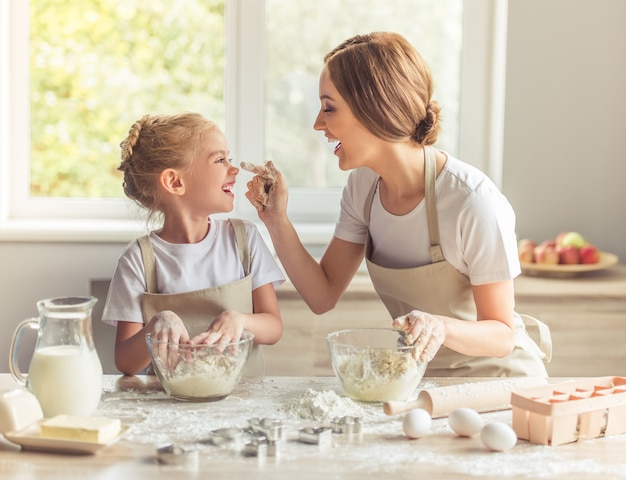 Cute little girl and her beautiful mom in aprons are playing