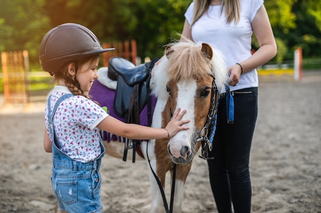 Cute little girl and her older sister enjoying with pony horse outdoors at ranch.