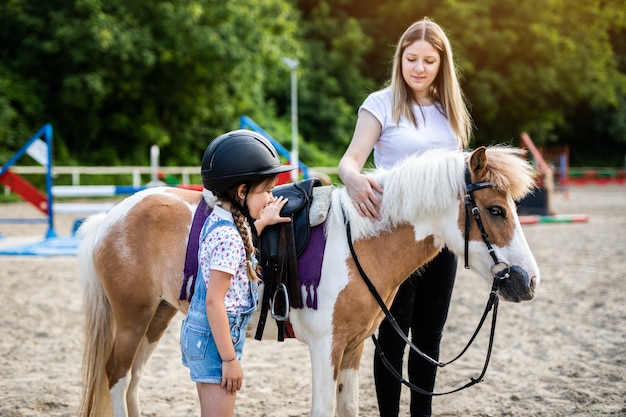 Cute little girl and her older sister enjoying with pony horse outdoors at ranch