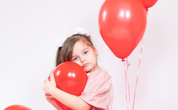 Cute little girl holding a bunch of red heartshaped balloons