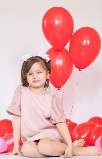 Cute little girl holding a bunch of red heartshaped balloons