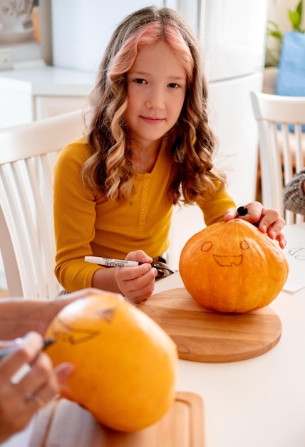 Cute little girl holding orange with spooky face sitting in kitchen Halloween lifestyle kid portrait Halloween preparations