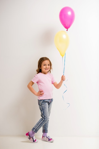 Cute little girl holding pink and yellow balloons.