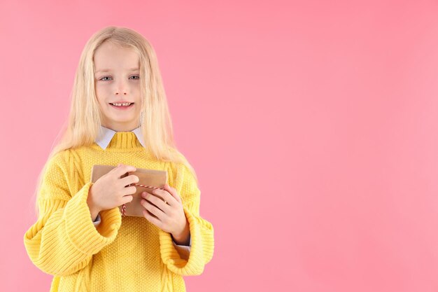 Cute little girl holds gift box on pink background