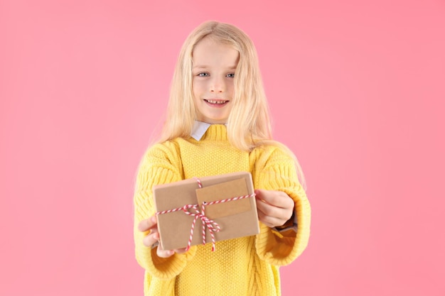 Cute little girl holds gift box on pink background