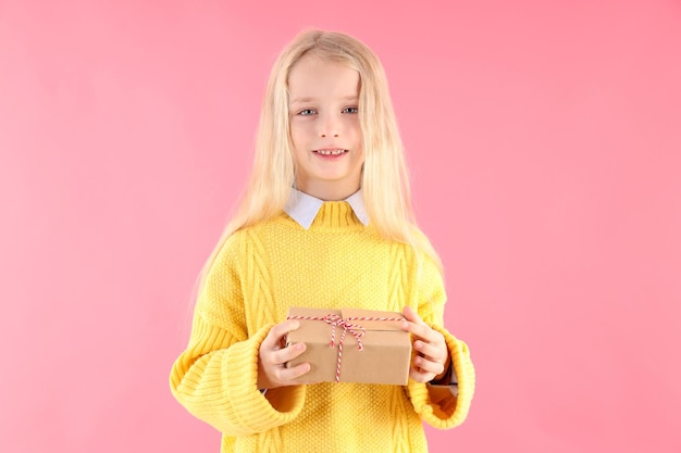 Cute little girl holds gift box on pink background