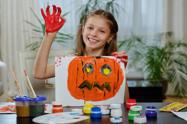 The cute little girl holds a poster with painted Halloween pumpkin.