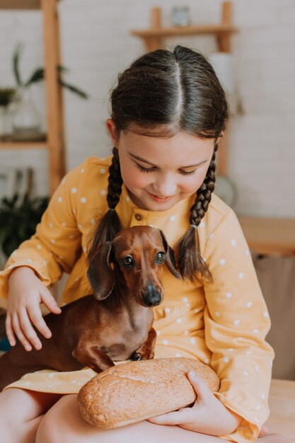 Cute little girl at home in the kitchen bakes cookies with her pet dog dachshund