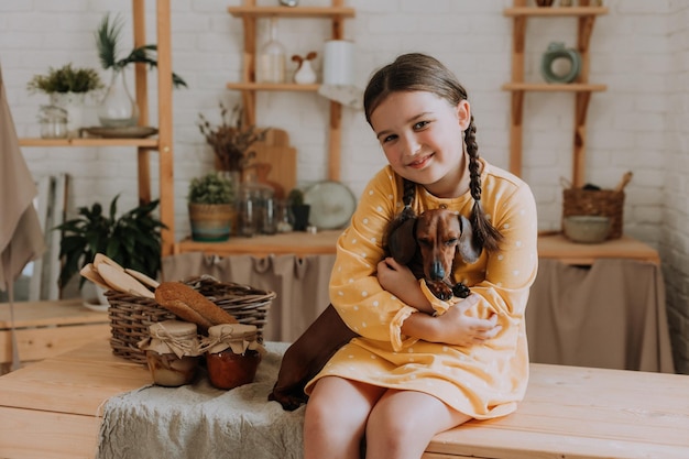 Cute little girl at home in the kitchen bakes cookies with her pet dog dachshund