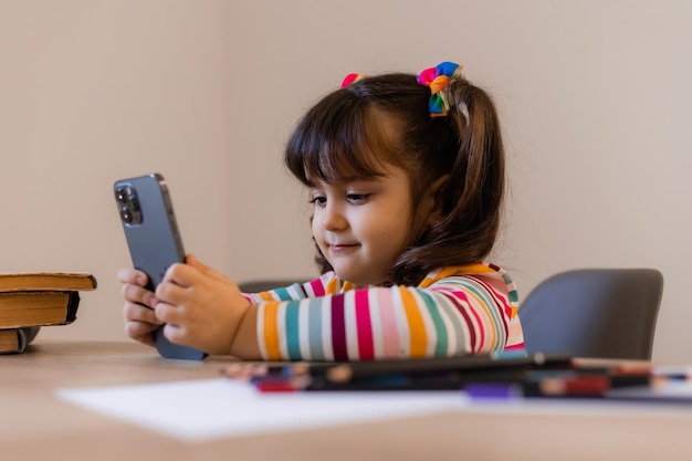 A cute little girl is engaged with a teacher online by phone Online education of children Preschoolers and gadgets