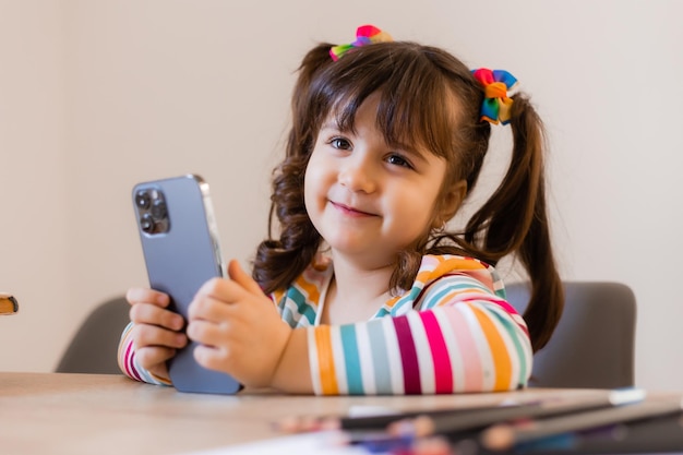 A cute little girl is engaged with a teacher online by phone Online education of children Preschoolers and gadgets