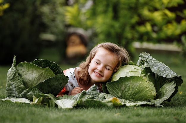 Cute little girl is having fun and lying on green grass near cabbages