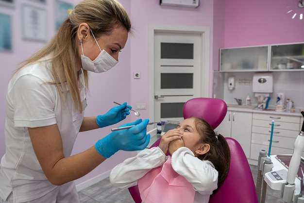 Cute little girl is sitting on the dental chair and does not want to treat her teeth by showing appropriate gestures concept of fear of dentists healthy oral cavity