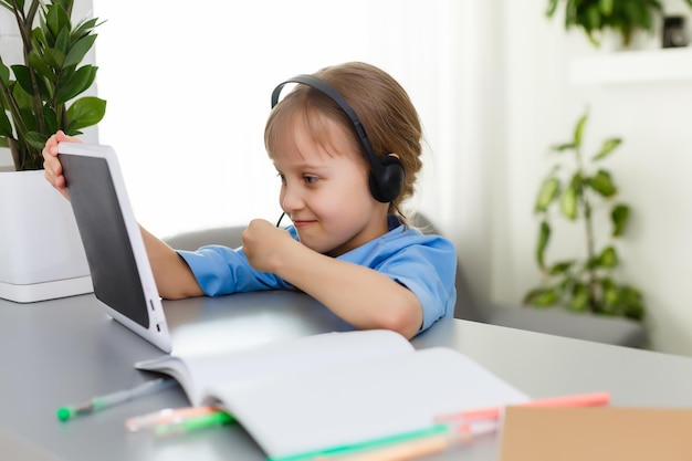 Cute little girl is sitting at table with her laptop and studying online