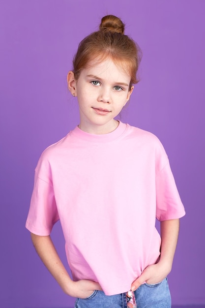 A cute little girl in jeans and a pink Tshirt on a purple background in the studio smiling grimacing and looking at the camera Children's games