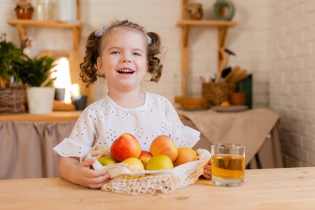 Cute little girl in the kitchen at home with apples and a glass of apple juice ecofriendly food for