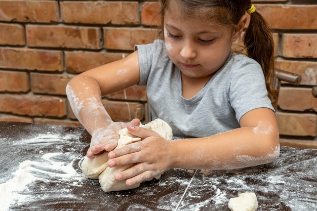 Cute little girl kneading dough, preparing dough for baking