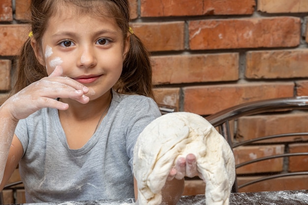 Cute little girl kneading dough, preparing dough for baking