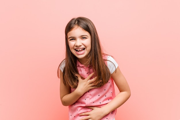 Cute little girl laughs happily and has fun keeping hands on stomach.