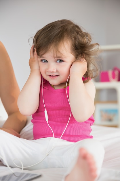 Cute little girl listening to music on bed