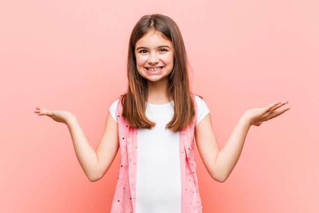 Cute little girl makes scale with arms, feels happy and confident.