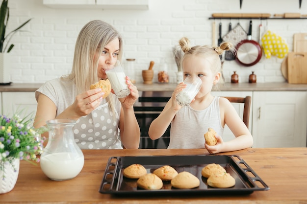 Cute little girl and mom eating freshly baked cookies with milk in the kitchen. Happy family. Toning.