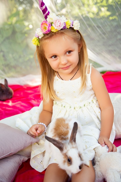 Cute little girl on nature in a unicorn hoop with rabbits.