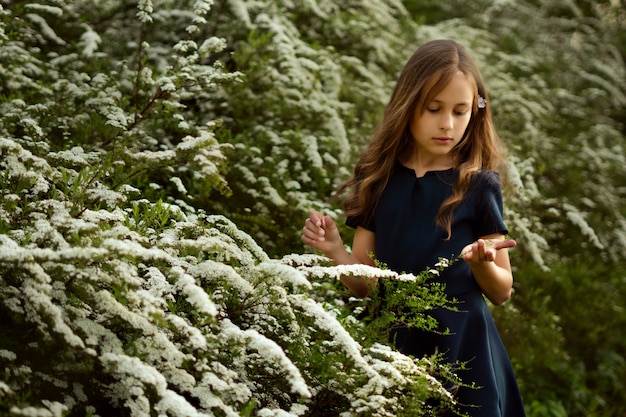 Cute little girl near beautiful white flowering bushes