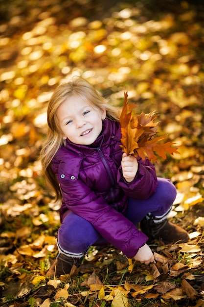 Cute Little girl in the park crouching with yellow leaves