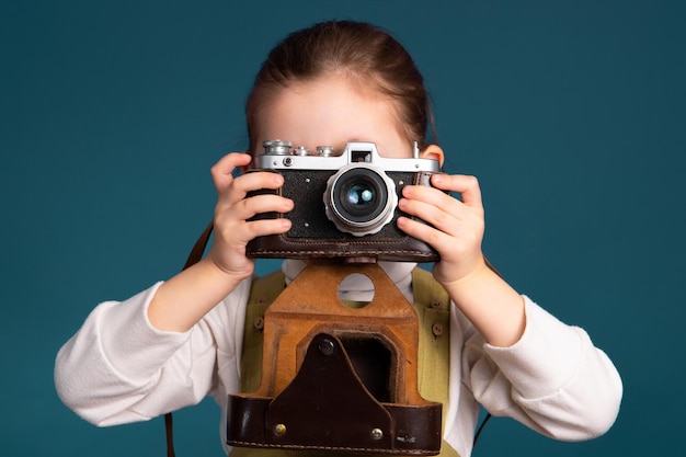 Cute little girl photographer taking pictures with retro camera Studio portrait on blue background